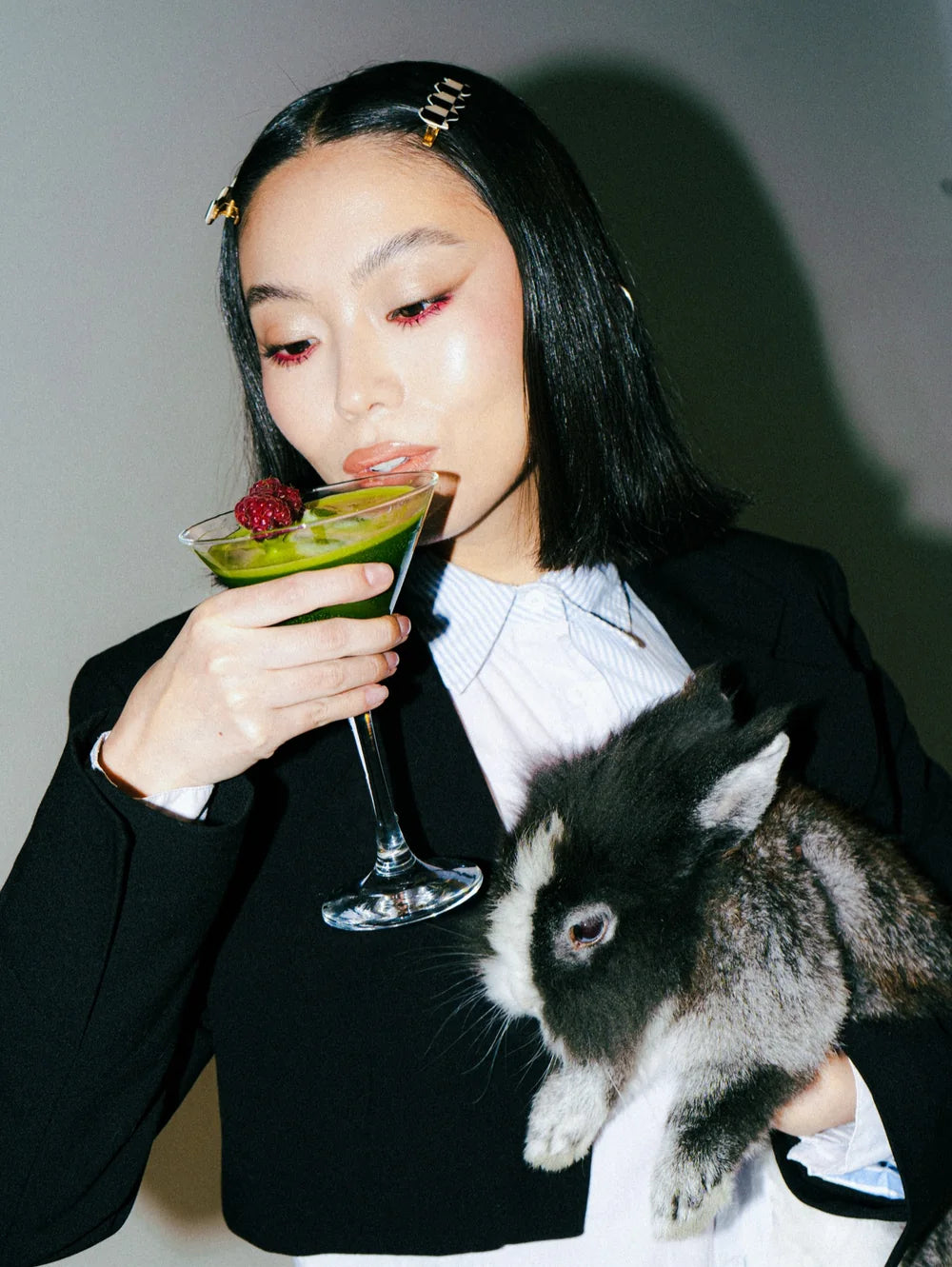 A model in black tailoring holding a vivid green matcha cocktail and a rabbit